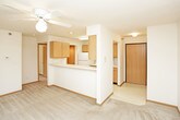 This single-floor unit is thoughtfully laid out to maximize functionality across its living spaces. The open living area is anchored by plush wall-to-wall carpeting and a ceiling fan with integrated lighting, creating a comfortable, airy atmosphere. A half-wall partition separates the living space from the kitchen, providing an open-concept feel while maintaining distinct zones.

The galley-style kitchen features warm oak cabinetry, white appliances including an electric range, built-in microwave, and refrigerator, along with light-toned countertops and vinyl tile flooring. A sliding-door closet adjacent to the kitchen provides convenient storage access.

The bedrooms are carpeted and well-proportioned, each featuring windows that admit natural light and views of the surrounding greenery. One bedroom includes a ceiling fan, while both offer access to closet storage. The neutral wall tones and wood-trimmed baseboards carry consistently throughout all rooms.

The bathroom is efficiently designed with a full tub-and-shower combination, a toilet, and a single-sink vanity topped with a wide mirror and illuminated by a bar light fixture. Vinyl tile flooring and clean white fixtures complete the space. Overall, the unit presents a clean, functional, and cohesive interior throughout.