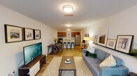 This single-floor residence offers a thoughtfully designed open-concept layout that seamlessly connects the living, dining, and kitchen areas. The living room is bright and welcoming, featuring large windows that allow ample natural light to fill the space, wood-look flooring, and a cozy seating arrangement centered around a flat-screen television. Adjacent to the living area, the dining space provides a dedicated spot for meals and gathering.

The kitchen is a functional highlight, showcasing warm-toned wood cabinetry, a full suite of stainless steel appliances including a refrigerator, range, microwave, and dishwasher, as well as a central island with bar seating — ideal for casual dining or entertaining. A clean entry corridor with wood-look flooring and coat hooks provides a practical transition into the main living space.

The bedroom is a comfortable retreat, featuring plush carpeting, a window with natural light, and convenient wall-mounted lighting. A full bathroom connects directly to the bedroom and includes a bathtub with shower, vanity with wood cabinetry, and wood-look flooring. Clean white walls throughout the residence create a bright, neutral backdrop that enhances the overall sense of openness and simplicity.