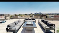 This rooftop terrace offers a well-appointed outdoor retreat with sweeping, unobstructed views of the Denver city skyline, surrounding neighborhoods, and the distant Rocky Mountains. The large-format tile flooring spans the entire deck, creating a clean, contemporary aesthetic that complements the modern design of the space.

The terrace is thoughtfully divided into distinct functional zones. A central lounge area features sleek, cushioned modular sofas and chairs arranged around a glass-topped fire pit table, ideal for relaxed gatherings. Potted ornamental grasses add touches of greenery throughout. A dedicated shaded dining area, covered by bold orange sail canopies stretched across a steel pergola structure, provides relief from direct sun while maintaining the open-air ambiance. High-top tables and chairs accommodate multiple guests, and a stainless steel gas grill is positioned nearby for outdoor cooking convenience.

Additional open space on the terrace allows for recreational activities, as evidenced by a cornhole board setup. White safety railings line the perimeter, framing panoramic views in every direction. The overall atmosphere is bright, airy, and urban, making the terrace a versatile space suited for both quiet relaxation and social entertaining.