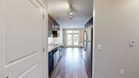 Located at 1520 Deford Bailey Ave in Nashville, TN, this two-bedroom, one-bathroom residence offers a well-designed single-floor layout that makes efficient use of its space. The galley-style kitchen is a standout feature, boasting dark espresso cabinetry extending from floor to ceiling, granite countertops, stainless steel appliances including a refrigerator, dishwasher, and range, and a classic tile backsplash. Track lighting illuminates the kitchen, which flows toward French doors that invite natural light into the living area and provide a view of the surroundings. Hardwood-style flooring runs throughout the main living areas, adding warmth and continuity to the open layout. The bedrooms are carpeted for comfort and feature neutral tones, ceiling fans, and generous windows that frame lush tree-lined views — the primary bedroom offering a particularly tranquil atmosphere. The bathroom is well-appointed with dark cabinetry, granite countertops, a large vanity mirror, tile flooring, and a soaking tub with tiled surround. A connecting hallway provides practical access between rooms, while a secondary space with wood-style flooring offers additional flexibility. The overall aesthetic is clean, modern, and move-in ready.