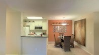 This single-floor residence offers a welcoming and well-appointed layout, highlighted by an open-concept design that seamlessly connects the kitchen and dining areas. The kitchen is outfitted with white cabinetry, dark countertops, and stainless steel appliances, including a built-in microwave and electric range, alongside a full-size refrigerator. A raised breakfast bar serves as a natural divider between the kitchen and the adjacent dining space, adding both functionality and visual interest. The dining area makes a striking impression with a bold terracotta accent wall, decorative plate wall art, and a shelf adorned with potted greenery. A pendant light fixture anchors the dining table, which is surrounded by woven rattan chairs, creating a warm and inviting atmosphere. Soft, neutral-toned carpeting flows through the living and dining spaces, contributing to a cozy ambiance. The textured ceiling and recessed flush lighting add to the finished character of the interior. Overall, the space strikes a balance between practical design and decorative charm, making it a comfortable and visually appealing environment.