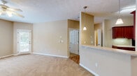 Located at 3300 Stadium Dr in Phenix City, Alabama, this single-floor residence offers a well-organized layout with one bedroom, one bathroom, and a combined kitchen and living area. The open-concept main living space features soft, neutral beige walls, plush carpet flooring, and a textured ceiling. A pendant light fixture hangs above the kitchen peninsula, which separates the kitchen from the living area and provides additional counter space. The kitchen is equipped with rich wood-toned cabinetry, light countertops, and black appliances including a refrigerator, range, and built-in microwave, all set over wood-look plank flooring that extends into the utility and entryway areas. The living room benefits from natural light through a windowed exterior door and offers a comfortable, open feel. The bedroom is a generously sized retreat featuring carpet flooring, a ceiling fan with light fixture, and a sliding glass door fitted with vertical blinds that opens to an outdoor view, bringing in abundant natural light. A dedicated closet provides convenient storage. The bathroom area connects to a utility space with washer/dryer hookups and louvered closet doors, adding practical functionality. Clean white trim and consistent warm-toned walls tie the entire space together cohesively.