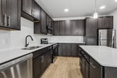 This 1,140-square-foot single-story unit offers a well-designed layout with 4 bedrooms, 2 bathrooms, and 1 kitchen. The modern kitchen is a standout feature, equipped with dark shaker-style cabinetry, white quartz countertops, stainless steel appliances including a refrigerator, range, microwave, and dishwasher, and a central island with pendant lighting overhead. Light hardwood flooring runs throughout the main living areas, adding warmth to the contemporary aesthetic. The four bedrooms are finished with plush carpeting, crisp white walls, and black-framed windows that invite natural light and offer open outdoor views of the surrounding landscape. The primary bedroom measures 180 square feet, providing a generous and comfortable retreat. Both bathrooms are finished with light tile flooring, dark cabinetry with white countertops, and matte black hardware accents. One bathroom features a walk-in shower, while the other includes a soaking tub and shower combination. Throughout the unit, clean lines, neutral tones, and consistent modern finishes create a cohesive and functional living environment suitable for a variety of occupants.