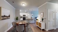 This single-floor residence in Pittsboro, North Carolina, offers a thoughtfully designed open-concept layout that seamlessly connects the kitchen, dining, and living areas. The kitchen is a functional centerpiece, featuring white shaker cabinetry, granite countertops, a tile backsplash, stainless steel appliances, and a large island with an integrated sink and bar seating — ideal for both cooking and casual dining. Pendant lighting above the island adds a polished touch, while recessed lighting and crown molding detail the ceilings throughout the main living areas.

The dining area accommodates a full-sized table and flows naturally into a comfortable living room, which benefits from natural light via window treatments. A welcoming entryway includes a granite-topped bench shelf and a wood-framed mirror, providing a practical transition space.

The bedrooms offer plush carpeting, ceiling fans, and natural light through slatted blinds. The bathroom features a granite vanity with a dark cabinet base, tile flooring, and a shower-tub combination. Hardwood-style flooring runs through the main living spaces, tying the design together with a warm, cohesive aesthetic throughout the home.