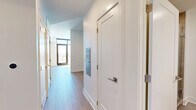 Located at 4096 Hillsboro Pike in Nashville, TN, this efficiently designed single-floor unit offers a thoughtful layout comprising a hallway, living room, kitchen, and bathroom. Light wood flooring runs throughout the main areas, lending warmth and visual continuity to the space.

The entry hallway is clean and bright, featuring white walls, gold-toned hardware accents, and access to the various rooms. It leads into an open living room bathed in natural light from a large glass door, creating an airy, welcoming atmosphere with track lighting overhead providing additional illumination.

The kitchen is a standout feature, showcasing a contemporary design with natural wood-toned lower cabinetry, matte gray upper cabinets, and a striking marble-patterned tile backsplash. White quartz countertops provide ample prep space, while stainless steel appliances — including a range, over-the-range microwave, dishwasher, and refrigerator — complete the modern aesthetic.

The bathroom continues the clean, modern design language with large-format neutral tile flooring, a wood-fronted vanity with a white countertop, and a walk-in shower with warm wood tile detailing. White walls and minimalist fixtures contribute to a calm, functional atmosphere throughout the space.