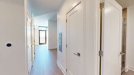 Located at 4096 Hillsboro Pike in Nashville, TN, this efficiently designed single-floor unit offers a thoughtful layout comprising a hallway, living room, kitchen, and bathroom. Light wood flooring runs throughout the main areas, lending warmth and visual continuity to the space.

The entry hallway is clean and bright, featuring white walls, gold-toned hardware accents, and access to the various rooms. It leads into an open living room bathed in natural light from a large glass door, creating an airy, welcoming atmosphere with track lighting overhead providing additional illumination.

The kitchen is a standout feature, showcasing a contemporary design with natural wood-toned lower cabinetry, matte gray upper cabinets, and a striking marble-patterned tile backsplash. White quartz countertops provide ample prep space, while stainless steel appliances — including a range, over-the-range microwave, dishwasher, and refrigerator — complete the modern aesthetic.

The bathroom continues the clean, modern design language with large-format neutral tile flooring, a wood-fronted vanity with a white countertop, and a walk-in shower with warm wood tile detailing. White walls and minimalist fixtures contribute to a calm, functional atmosphere throughout the space.