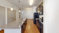Located at 2120 Waterside Cir. in Graham, North Carolina, this single-floor residence offers a thoughtfully designed open-concept layout that seamlessly connects the kitchen, dining, and living areas. The kitchen is a standout feature, showcasing dark espresso cabinetry, granite countertops, a spacious island with a built-in sink, and black appliances including a refrigerator, range, and over-the-range microwave. Pendant lighting adds a stylish touch above the island, enhancing the kitchen's functional elegance. Adjacent to the kitchen, the dining area benefits from additional pendant lighting and direct sightlines to the living space, creating a cohesive flow throughout the unit. The living room is bright and airy, filled with natural light streaming through large windows, and is equipped with a ceiling fan for added comfort. Warm wood-style flooring runs consistently throughout the entire space, lending a clean and unified aesthetic. The bathroom features a double-sink vanity with granite countertops and dark cabinetry, a large mirror, and a soaking tub with a tiled surround. Additional storage and closet space are visible throughout, contributing to the residence's practical and livable design.