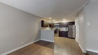 This single-floor unit offers a thoughtfully designed open-concept layout that seamlessly connects the living area and kitchen. The kitchen stands as a highlight of the space, showcasing rich dark espresso cabinetry with sleek chrome hardware, light granite countertops, and a striking mosaic tile backsplash that adds a modern, textured accent. A full suite of stainless steel appliances — including a refrigerator, electric range, and over-the-range microwave — enhances the kitchen's contemporary appeal. A raised peninsula provides a natural divide between the kitchen and the open living area, offering additional counter space and serving as an ideal casual dining spot. Warm wood-look flooring flows consistently throughout the unit, providing both durability and a cohesive aesthetic. The textured ceiling adds a classic finishing touch. The bedroom is a comfortable, well-proportioned room with the same wood-look flooring, neutral walls, and a window fitted with blinds that allow for natural light and privacy. The bathroom features a clean, functional design with a tiled tub-shower combination, a dark vanity with granite countertop, chrome fixtures, and wood-look flooring that ties the space together. Overall, the unit presents a modern, move-in-ready feel with consistent finishes throughout.