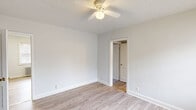 This single-floor unit offers a practical and functional layout across three bedrooms, one bathroom, a kitchen, and a closet. The interior is finished with a clean, neutral palette of white and light gray tones throughout, creating a bright and airy atmosphere.

Two of the bedrooms feature light wood-style laminate flooring, textured ceilings, and ceiling fans with integrated lighting, providing both comfort and airflow. These rooms share a similar open, uncluttered feel with white-trimmed doorways connecting to the rest of the unit. The third bedroom is carpeted and benefits from two windows fitted with blinds, allowing natural light to filter in, alongside a classic cast-iron radiator that serves as a heating source.

The kitchen is efficiently designed with white upper and lower cabinetry, light countertops, a stainless steel sink, and black appliances including a gas range and refrigerator. A window with blinds and a radiator unit add natural light and warmth to the space.

The bathroom is neatly appointed with a vanity, mirror, toilet, a walk-in shower stall, wood-style flooring, and a window for ventilation. A radiator is also present, ensuring consistent warmth.

The entry area features a classic paneled door, a ceiling fan, wood-style flooring, an open closet, and a radiator, providing a welcoming introduction to the unit.