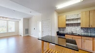 This single-floor residence offers a thoughtfully designed layout across two bedrooms and two bathrooms. The open living room is a bright, welcoming space anchored by warm hardwood-style flooring and a large triple-pane window that fills the room with natural light and frames views of the surrounding neighborhood. Track lighting overhead adds a modern touch to the airy interior.

The kitchen is well-equipped with light wood cabinetry, dark granite countertops, stainless steel appliances including a refrigerator and range, and a striking mosaic tile backsplash in grey and white tones. A kitchen island with a matching granite surface adds additional prep and dining space.

The primary bedroom features plush carpeting, neutral walls, and a generous window with outdoor views, creating a calm and restful retreat. The second bedroom, also carpeted, is a comfortable and versatile space with its own window allowing natural light.

The primary bathroom is fitted with a double-sink vanity topped with dark granite, light wood cabinetry, tile flooring, and access to a walk-in closet. The second bathroom features a clean, walk-in shower with chrome fixtures and hardwood-style flooring. A connecting hallway ties the layout together cohesively, making this a practical and attractive living space.