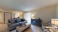 This single-floor residence offers a well-organized layout that balances comfort and functionality across several distinct living areas. The living room serves as the heart of the home, featuring plush wall-to-wall carpeting, neutral wall tones, and a textured ceiling. A large sliding glass door fitted with vertical blinds draws in natural light and provides access to the outdoors. The room offers generous space for seating arrangements and additional storage furnishings.

Adjacent to the living room, a defined dining area provides an intimate setting for meals, comfortably accommodating a four-seat table. The galley-style kitchen is outfitted with warm wood cabinetry, white countertops, tile flooring, and includes a dishwasher, offering efficient use of space along parallel walls.

The primary bedroom is a well-proportioned retreat with soft carpeting, neutral walls, and direct access to an adjoining room. A secondary bedroom features a window for natural light and includes a walk-in closet, offering practical storage. The full bathroom is finished with a wood-toned vanity, light stone-style countertop, a shower-tub combination, and tile flooring, maintaining a clean and cohesive aesthetic throughout.