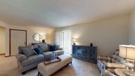 This single-floor residence offers a well-organized layout that balances comfort and functionality across several distinct living areas. The living room serves as the heart of the home, featuring plush wall-to-wall carpeting, neutral wall tones, and a textured ceiling. A large sliding glass door fitted with vertical blinds draws in natural light and provides access to the outdoors. The room offers generous space for seating arrangements and additional storage furnishings.

Adjacent to the living room, a defined dining area provides an intimate setting for meals, comfortably accommodating a four-seat table. The galley-style kitchen is outfitted with warm wood cabinetry, white countertops, tile flooring, and includes a dishwasher, offering efficient use of space along parallel walls.

The primary bedroom is a well-proportioned retreat with soft carpeting, neutral walls, and direct access to an adjoining room. A secondary bedroom features a window for natural light and includes a walk-in closet, offering practical storage. The full bathroom is finished with a wood-toned vanity, light stone-style countertop, a shower-tub combination, and tile flooring, maintaining a clean and cohesive aesthetic throughout.