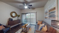 This single-floor residence offers a thoughtfully designed layout that balances comfort and functionality. The living area is a welcoming focal point, featuring rich dark hardwood-style flooring, a ceiling fan with integrated lighting, and a large sliding glass door fitted with vertical blinds that opens to a private balcony with outdoor views — filling the space with natural light.

The open-concept kitchen is well-equipped with rich dark wood cabinetry, a center island with bar seating, pendant and track lighting, and black appliances. A separate dining area with additional bar-height seating complements the kitchen, creating a seamless space for entertaining.

The bedroom is a comfortable retreat with plush carpeting, a ceiling fan, and a generously sized window that frames views of the surrounding greenery. It connects to a spacious walk-in closet outfitted with wire shelving and hanging rods for ample storage.

The bathroom features warm wood cabinetry with a wide vanity, stone-toned countertops, a large framed mirror, and hardwood-style flooring. Throughout the residence, neutral tones and consistent finishes create a cohesive, modern aesthetic that is both inviting and practical.