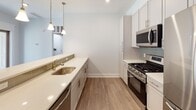 Located at 919 Sunnyview Oval in Fords, NJ, this thoughtfully designed one-bedroom, one-bathroom residence offers a clean, modern aesthetic throughout its single-floor layout. The open-concept kitchen is a standout feature, showcasing white shaker-style cabinetry, quartz countertops, a subway tile backsplash, and a full suite of stainless steel appliances including a gas range, built-in microwave, refrigerator, and dishwasher. A large peninsula with beadboard detailing and pendant lighting above creates a natural divide between the kitchen and the spacious living area, which is outfitted with recessed lighting, a ceiling fan, and a sliding glass door that invites natural light into the space. Light-toned wood-style flooring flows consistently throughout, adding warmth and cohesion. The bedroom is generously sized, featuring crown molding, a ceiling fan, a window with outdoor views, and access to a walk-in closet. The full bathroom is well-appointed with a dual-sink vanity, quartz counters, a large mirror, and a tiled tub-shower combination. An in-unit stacked washer and dryer provides added everyday convenience, completing this well-equipped and move-in-ready residence.