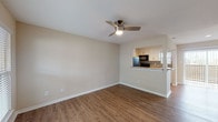 This single-floor residence offers a clean, contemporary layout designed for comfortable everyday living. The open living area is finished with warm wood-look flooring and neutral beige walls, creating a welcoming atmosphere throughout. A ceiling fan with a built-in light fixture provides both comfort and illumination. A large window and entry door allow natural light to fill the space, while a pass-through counter connects the living area to the kitchen, enhancing the sense of openness.

The kitchen is efficiently designed with white cabinetry, light butcher-block-style countertops, a stone tile backsplash, and black appliances including a refrigerator, electric range, microwave, and dishwasher. Wood-look flooring continues seamlessly into the kitchen.

The bedrooms are generously sized, each featuring ceiling fans, wood-look flooring, and windows with blinds that provide natural light and privacy. The primary bedroom includes access to a closet and an en-suite bathroom. Additional closet space is also visible in the layout.

The bathroom is tastefully finished with large-format beige tiles lining the shower-tub combination, accented by a decorative mosaic tile border. Chrome fixtures and wood-look flooring complete the space. Overall, the residence presents a cohesive, move-in-ready interior with practical finishes throughout.