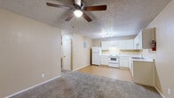 This single-floor unit offers a practical and functional layout with a seamless open-concept design connecting the living area and kitchen. The living room features neutral-toned carpet, a ceiling fan with integrated lighting, and a textured ceiling, creating a comfortable and casual atmosphere. It flows directly into the kitchen, which transitions to light wood-look flooring and is equipped with white cabinetry, a white appliance suite including a refrigerator, electric range, and dishwasher, along with a double-basin sink and ample counter space. A track lighting fixture brightens the kitchen area effectively. The electrical panel is conveniently located within the kitchen zone. The bedrooms are carpeted and each include ceiling fans, offering a cozy feel. One bedroom features a walk-in closet with a rod and shelving system, while windows fitted with horizontal blinds provide natural light throughout. The bathroom includes a vanity with a speckled countertop, an integrated sink, white cabinetry below, and a framed mirror above. Warm beige tones are carried consistently across the walls throughout the unit, contributing to a cohesive and neutral interior palette.
