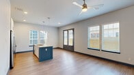 This single-floor residence combines modern design with practical living across a well-organized open layout. The heart of the home is a bright, open-concept kitchen and living area, unified by warm wood-tone luxury vinyl plank flooring. The kitchen features a standout two-tone island with a bold blue base, granite countertops, and an undermount sink, complemented by white upper cabinetry and a full suite of stainless steel appliances including a French door refrigerator, range, and microwave. Pendant lighting above the island adds a contemporary accent. The adjoining living area is generously sized, bathed in natural light from multiple windows fitted with blinds, and centered under a modern ceiling fan. A set of dark-framed French doors opens to the exterior, enhancing both the light and the connection to the outdoors. The bedroom offers plush carpeting, tall ceilings, a ceiling fan, and ample natural light from dual windows, with convenient closet access via a paneled gray door. The bathroom is well-appointed with a white vanity, granite countertop, undermount sink, and a large framed mirror. Consistent navy blue baseboards throughout the space tie the design together, creating a cohesive and polished aesthetic.