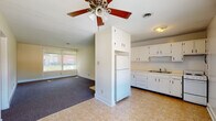 This single-floor unit on Forest Hill Drive in Frankfort, Kentucky, offers a straightforward, functional layout designed for comfortable everyday living. The open-concept kitchen and living area serve as the heart of the space, where tile flooring transitions seamlessly into carpeted living space. The kitchen is equipped with ample white cabinetry extending to the ceiling, a double-basin sink, a white electric range, and a full-size refrigerator positioned within a built-in column that also serves as a natural divider between the kitchen and living areas. A ceiling fan with a light fixture overhead adds both comfort and practicality to this shared space.

The living area is generously proportioned, with neutral-toned walls, plush carpet, and a large window that brings in natural light and outdoor views. Additional rooms, also carpeted and finished with the same warm neutral palette, feature multiple windows dressed with horizontal blinds, allowing for adjustable natural light throughout the day. The bathroom includes a full tub-shower combination with white tile surround, a toilet, a vanity with storage, tile flooring, and a window for ventilation. Overall, the space presents a clean, no-frills design with consistent finishes throughout.