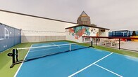 Located in the heart of Uptown Charlotte at 426 N Tryon St, Trella Uptown is a vibrant rooftop recreational venue that combines sport, socializing, and striking urban scenery. The facility centers around multiple blue-surfaced pickleball courts enclosed by chain-link fencing, offering a well-maintained playing environment with court lighting for extended hours of play. Adjacent to the courts, a basketball hoop provides additional athletic options.

The social areas are thoughtfully designed and visually energetic. Lush artificial turf sections are furnished with Adirondack chairs, side tables, and cornhole boards, creating relaxed gathering spots ideal for spectators and socializers alike. Vibrant large-format planters in bold yellow and natural tones add greenery and color throughout the space.

A hardscape patio area features picnic-style bench seating alongside grills, making it suitable for group events and casual dining. Pergola structures offer shaded retreats, while string lights draped across the venue add warmth to the atmosphere after dark. A bold, colorful mural decorates the exterior building wall, reinforcing the venue's playful and lively character.

Throughout the space, panoramic views of the Charlotte skyline — including prominent Uptown skyscrapers — serve as a dramatic backdrop, making Trella Uptown a distinctive destination for both competitive play and social gatherings.