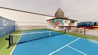 Located in the heart of Uptown Charlotte at 426 N Tryon St, Trella Uptown is a vibrant rooftop recreational venue that combines sport, socializing, and striking urban scenery. The facility centers around multiple blue-surfaced pickleball courts enclosed by chain-link fencing, offering a well-maintained playing environment with court lighting for extended hours of play. Adjacent to the courts, a basketball hoop provides additional athletic options.

The social areas are thoughtfully designed and visually energetic. Lush artificial turf sections are furnished with Adirondack chairs, side tables, and cornhole boards, creating relaxed gathering spots ideal for spectators and socializers alike. Vibrant large-format planters in bold yellow and natural tones add greenery and color throughout the space.

A hardscape patio area features picnic-style bench seating alongside grills, making it suitable for group events and casual dining. Pergola structures offer shaded retreats, while string lights draped across the venue add warmth to the atmosphere after dark. A bold, colorful mural decorates the exterior building wall, reinforcing the venue's playful and lively character.

Throughout the space, panoramic views of the Charlotte skyline — including prominent Uptown skyscrapers — serve as a dramatic backdrop, making Trella Uptown a distinctive destination for both competitive play and social gatherings.