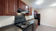 Located at 209 W Lockhaven Dr in Goldsboro, NC, this two-floor property offers a practical and well-maintained layout throughout. The kitchen is a functional centerpiece, featuring rich dark-wood cabinetry with raised-panel detailing, dark granite-style countertops, and a full suite of black appliances including a coil-burner electric range, refrigerator, and dishwasher. A stainless steel sink sits beneath a window, allowing natural light into the space, while a range hood and ample upper and lower cabinet storage add to its utility. Light wood-look vinyl plank flooring runs through the main living areas, providing a clean, durable surface. The living room is generously proportioned, highlighted by a ceiling fan, a sliding glass door that invites natural light and outdoor views, and direct access to adjacent rooms. A textured ceiling is consistent throughout. The bedrooms are finished with soft, neutral carpet and feature windows with blinds, providing a quiet and comfortable retreat. One bedroom includes access to an additional room or closet space. The bathroom includes a full soaking tub and shower combination with chrome fixtures and clean white surround. A folding door closet and built-in HVAC vents are also present throughout the home, contributing to its efficient design.