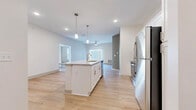 Located at 6386 Transit Rd in Depew, NY, this single-floor unit offers a clean, modern design with an open and airy layout throughout. The heart of the home is a well-appointed kitchen featuring a central island with a granite countertop, undermount sink, and pendant lighting overhead. White shaker-style cabinetry, a subway tile backsplash, and a full suite of stainless steel appliances — including a refrigerator, range, and microwave — complete the space. Light hardwood flooring flows seamlessly through the kitchen and into the open living area, which is bathed in natural light from large windows and a sliding glass door fitted with vertical blinds. A ceiling fan adds comfort to the living area. The bedrooms are carpeted for warmth and comfort, each featuring ceiling fans and windows that bring in natural light. The primary suite includes a walk-in closet with wire shelving for organized storage. The bathroom is finished with hardwood-style flooring and includes a walk-in shower. Throughout the unit, neutral wall tones and recessed lighting create a bright, cohesive atmosphere that is both functional and inviting.
