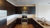 Located along West Fourth Street Extension in Charlotte, NC, this single-floor residence offers a thoughtfully designed layout with modern finishes throughout. The kitchen is a standout feature, equipped with a full suite of stainless steel appliances—including a French door refrigerator with ice maker, electric range, and over-the-range microwave—complemented by rich dark cabinetry extending to the ceiling for generous storage. Granite countertops provide ample workspace, and hardwood-style flooring runs consistently throughout the main living areas, adding warmth and cohesion.

The living area is bright and open, with multiple windows fitted with horizontal blinds allowing for adjustable natural light. A ceiling fan enhances comfort, and sliding glass doors lead to a private balcony with views of surrounding greenery. The bedroom is similarly well-lit, featuring a bank of windows and a ceiling fan, with direct access to a walk-in closet outfitted with wire shelving on multiple levels for organized storage. The bathroom includes a soaking tub with a tiled surround and brushed nickel fixtures, offering a clean, functional aesthetic. Light neutral wall tones and consistent flooring unify the space throughout.