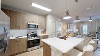 Located at 1875 Maple Dr in Kennesaw, GA, this thoughtfully designed 2-bedroom, 2-bathroom residence offers a cohesive modern aesthetic across its single floor. The open-concept kitchen and living area serves as the heart of the home, where light wood-tone cabinetry extends floor to ceiling alongside stainless steel appliances, including a range, microwave, and French door refrigerator. A quartz-topped island with an undermount sink and seating for two anchors the kitchen, illuminated by brushed nickel pendant lights. Light wood-look flooring flows seamlessly from the kitchen into the living room, which features large windows that invite abundant natural light and a ceiling fan overhead. The primary bedroom offers a comfortable, carpeted retreat with a generous walk-in closet outfitted with built-in shelving and hanging rods. Both bathrooms are finished with warm wood vanities, white quartz countertops, and frameless glass shower enclosures with wood-look tile flooring. A second well-proportioned bedroom also benefits from natural light. Throughout, a neutral warm-gray palette, clean architectural lines, and quality finishes create a refined, move-in-ready living environment.