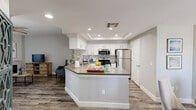 Located in Phoenix, AZ, this 2-bedroom, 1-bathroom home offers a well-appointed single-level layout with modern finishes throughout. The open-concept kitchen and living area serves as the heart of the home, featuring white shaker cabinetry, subway tile backsplash, stainless steel appliances including a gas range, microwave, and refrigerator, and a wraparound peninsula with a built-in sink and neutral countertops. A tray ceiling with recessed lighting adds architectural interest to the kitchen. Wood-style flooring flows seamlessly through the main living areas, complementing the bright, neutral color palette. The living room is anchored by a tiled fireplace and sliding glass doors that invite abundant natural light while providing access to an outdoor space. A ceiling fan enhances comfort throughout the room. Both bedrooms are carpeted and fitted with ceiling fans, offering a quiet retreat. The primary bedroom is generously sized and connects to a spacious walk-in closet with multi-tiered shelving and hanging rods. The full bathroom features a wide vanity with white cabinetry, a large mirror, and wood-style flooring. The overall aesthetic is clean, contemporary, and move-in ready.