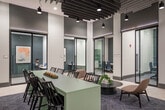 Located at 3 Hawkins Ave in Ronkonkoma, NY, these office rooms offer a thoughtfully designed, single-floor workspace that balances open collaboration with private functionality. The layout encompasses a generous footprint, providing ample room for a variety of work settings and configurations.

The open common area serves as the heart of the space, featuring a long communal bar-height table with seating, ideal for casual meetings or shared work sessions. A separate lounge zone offers comfortable chairs and a round coffee table atop a geometric-patterned area rug, encouraging informal gatherings. A dedicated refreshment station, set against a striking geometric-tiled accent wall in muted teal and white tones, is equipped with a coffee machine and counter space with cabinetry.

Glass-walled, black-framed conference rooms line the perimeter, offering visual connectivity while maintaining acoustic privacy. These enclosed rooms are outfitted with conference tables and seating for focused meetings. Secluded high-back lounge pods provide additional private nooks for individual work or small discussions.

Soaring ceilings with exposed industrial-style baffle panels and pendant lighting lend the space a contemporary, polished aesthetic. Light tile flooring transitions to patterned carpet in seating areas, adding warmth and definition. A corridor with arched architectural detailing connects to elevator access, completing this well-appointed professional environment.