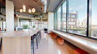 Located at 30 Peabody Street in Nashville, Tennessee, this contemporary office suite occupies a single floor and offers a thoughtfully designed workspace blending industrial aesthetics with modern comfort. The open common areas feature polished concrete floors, exposed ductwork, soaring ceilings, and floor-to-ceiling windows that flood the space with natural light and frame sweeping views of the Nashville skyline and the iconic Korean Veterans Memorial Bridge. A communal bar-height island with bar seating serves as a central gathering point, complemented by lounge seating areas with warm-toned furnishings, built-in banquette seating, and decorative acoustic ceiling panels. The suite includes 13 private offices, each finished with quality furnishings and large windows offering city and river views. A well-appointed lounge area features a mix of booth-style seating and soft lounge chairs, creating a relaxed yet professional atmosphere. The spacious outdoor patio is a standout amenity, equipped with stylish seating arrangements, high-top bar tables, and open-sky views of the Nashville cityscape — ideal for breaks or informal meetings. Throughout, the design balances an industrial-modern character with refined, hospitality-inspired touches.