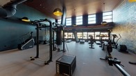 Located at 1270 4th Street NE in Washington DC, The Batley fitness center is a thoughtfully designed, single-floor gym that seamlessly combines industrial aesthetics with high-end fitness amenities. The space is anchored by a striking feature wall of dark teal brick adorned with intricate gold leaf-pattern artwork, creating a bold visual centerpiece throughout the facility.

The cardio zone is well-appointed with a row of treadmills, ellipticals, and stair climbers, bathed in natural light from a generous bank of tall windows. Exposed ductwork and pendant lighting with warm gold-toned interiors complement the deep teal and terracotta color palette, lending the space an urban, contemporary character.

The strength and functional training area features power racks, cable machines, adjustable benches, and a punching bag, alongside plyometric boxes for versatile workout options. A dedicated studio room offers hardwood flooring, wall-to-wall mirrors, a ballet barre, and a rack of medicine balls — ideal for flexibility, balance, and functional training sessions.

Pendant dome lights in matte black and gold are distributed throughout, maintaining consistent, focused illumination across all zones. The Batley branding is subtly incorporated via signage, reinforcing the facility's cohesive identity. Overall, the space delivers a premium fitness environment with a refined, design-forward atmosphere.