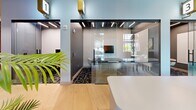 Located at 147 W Wood St in West Lafayette, Indiana, this single-floor commercial space offers a thoughtfully designed and modern work environment. The layout includes a welcoming reception area anchored by a sleek white curved desk, light hardwood flooring, and lush tropical plants that add a refreshing organic touch to the contemporary aesthetic.

Glass-walled meeting rooms line the hallways, offering transparency and an open feel while maintaining functional separation. Each meeting room is outfitted with a light wood conference table, comfortable upholstered chairs, and bold graphic accent walls featuring an artistic collage-style mural in muted gold, black, and white tones. Linear LED ceiling fixtures provide consistent, professional illumination throughout.

One of the meeting rooms features a wall-mounted flat-screen display and a built-in whiteboard, making it well-suited for presentations and collaborative sessions. The patterned dark carpet in the meeting rooms contrasts smartly with the hardwood flooring in the common areas.

The main lounge or collaboration zone benefits from large windows dressed with warm amber curtains, allowing natural light to filter in while adding a rich color accent. Open shelving with greenery and stylish pendant lighting complete the inviting atmosphere. Numbered room identifiers with gold accents add a refined, organized touch to the overall design.
