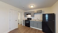 Located at 12702 Blue Ridge Circle in Grandview, Missouri, this single-floor unit offers a clean, updated interior with a cohesive design throughout. Durable hardwood-style plank flooring runs continuously across the living, kitchen, and bedroom areas, providing a unified and easy-to-maintain aesthetic.

The kitchen is a standout feature, equipped with gray shaker-style cabinetry, granite-look countertops, a white subway tile backsplash, and black appliances including an electric range and full-size refrigerator. An under-cabinet range hood and a single-basin sink with modern faucet complete the functional layout. The kitchen opens directly to the living area, creating an efficient, open flow.

The living area is bright and spacious, featuring a textured ceiling, a wall-mounted HVAC unit, and a front entry door with an adjacent window that allows natural light to fill the room. A ceiling fan with light fixture adds comfort to the space.

The bedroom is well-proportioned, featuring a ceiling fan, a window with blinds, a closet with double panel doors, and direct access to the bathroom. The bathroom includes a vanity with a mirror, a full soaking tub with shower surround, a toilet, and coordinating gray cabinetry consistent with the kitchen design. The textured ceilings present throughout add a consistent architectural detail to the entire unit.