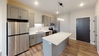 Located at 223 Roberts St N in Fargo, North Dakota, this single-floor unit offers a thoughtfully designed layout with contemporary finishes throughout. The open-concept kitchen serves as a central highlight, featuring gray shaker-style cabinetry with black hardware, white quartz countertops, and a chevron-patterned tile backsplash. A center island provides additional prep and seating space, while pendant lighting with a cluster globe fixture adds a stylish focal point. Stainless steel appliances, including a refrigerator, range, microwave, and dishwasher, complete the kitchen. Wood-look plank flooring runs throughout the main living areas, contributing warmth and continuity across the space. The living area benefits from natural light through a pair of windows offering views of the surrounding Fargo cityscape. The bathroom is finished with marble-style tile flooring, a wide vanity with a white quartz countertop, an undermount sink, a large mirror with overhead lighting, and a recessed medicine cabinet. Gray shaker-style cabinetry ties the bathroom design back to the kitchen aesthetic, creating a cohesive look. The overall ambiance is clean, modern, and move-in ready.