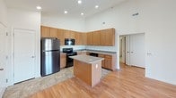 This single-floor residence is thoughtfully designed to balance open communal spaces with comfortable private retreats. At the heart of the home, the kitchen commands attention with its impressively high ceilings, warm honey-toned cabinetry extending nearly to the ceiling, and granite-look countertops. A central island provides additional prep space and casual gathering potential. Stainless steel appliances, including a refrigerator, electric range with over-the-range microwave, and dishwasher, complete the functional layout. The kitchen flows seamlessly into the adjacent living area, which features light-toned hardwood flooring and a large sliding door that invites natural light and outdoor views. The bedrooms are finished with plush wall-to-wall carpeting, ceiling fans with light fixtures, and generously sized windows that fill each room with natural light. At least one bedroom includes a spacious walk-in closet with built-in shelving. The full bathroom is well-appointed with warm wood-toned cabinetry, a backlit vanity mirror, stone-tile flooring, and a full tub-shower combination with white subway tile surround. An adjacent walk-in closet or linen storage area adds further practicality. Throughout, the space maintains a clean, neutral palette that enhances its bright and airy ambiance.