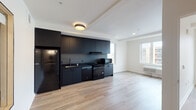 Located at 5620 N Interstate Avenue in Portland, Oregon, this single-floor unit delivers a clean, contemporary design throughout. The open-concept living and kitchen area is anchored by a striking matte-black kitchen, featuring floor-to-ceiling cabinetry, black countertops, and a full suite of black appliances including a refrigerator, dishwasher, range, and microwave. Light-toned hardwood flooring runs throughout the main living spaces, creating a warm contrast against the dark kitchen aesthetic. Natural light filters in through large windows, brightening the open living area and lending an airy feel to the space. The bedroom is well-proportioned with its own large window offering views of the surrounding Portland neighborhood, a wall-mounted mini-split unit for climate control, and access to a walk-in closet with built-in wire shelving via sliding bypass doors. The bathroom presents a clean, minimalist design with a wall-mounted sink, a mirror medicine cabinet, a soaking tub, and dark tile flooring complemented by matte black fixtures and hardware. An in-unit laundry area adds everyday convenience. Overall, the space combines modern industrial aesthetics with functional, thoughtfully designed living areas.