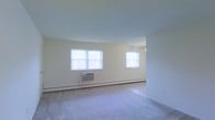 Located at 760 Eayrestown Road in Lumbertown, NJ, this single-floor unit offers a straightforward and functional layout designed for comfortable everyday living. The main living area is finished with wall-to-wall carpeting underfoot, lending a warm and quiet atmosphere to the space. Two generously sized windows allow ample natural light to fill the room, creating a bright and airy feel throughout the day. A window-mounted air conditioning unit provides cooling during warmer months, while baseboard heating ensures consistent warmth throughout the colder seasons. A ceiling fan is also present, contributing to year-round climate comfort. The neutral-toned walls offer a clean, versatile backdrop that accommodates a variety of furnishing and décor styles. The open feel of the living area provides flexibility in how the space can be arranged and utilized. The overall ambiance is simple, practical, and well-lit, making it a functional residence suited for those seeking an easy-to-maintain living space in a residential setting in Burlington County, New Jersey.