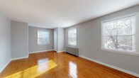 Located at 1358 Elbur Ave in Lakewood, Ohio, this single-floor home offers a clean, functional layout with consistent design details throughout. Polished hardwood floors extend across the main living areas and bedrooms, reflecting natural light and lending warmth to the neutral gray-painted walls.

The spacious living area is bright and open, featuring multiple white-framed windows that invite ample sunlight. A classic cast-iron radiator provides efficient heating, complementing the home's traditional character. An additional room, suitable as a bedroom, mirrors this layout with its own set of windows, ceiling fan with light fixture, and radiator — offering both comfort and ventilation.

The kitchen is efficiently designed with white cabinetry, dark countertops, a gas range, a full-size refrigerator, a sink with a window above it, and a radiator. Track lighting illuminates the space, and light tile flooring provides a practical, easy-to-maintain surface.

The bathroom is neatly appointed with tile flooring, a pedestal-style sink, toilet, and a shower with a window for natural light and ventilation. White finishes throughout maintain a clean, cohesive look.

An additional room off the main living area features its own entry door, offering flexible use as a bedroom, office, or den. Throughout the home, bright windows, well-maintained hardwood floors, and classic architectural details create a welcoming and functional living environment.