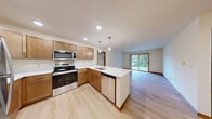 Located at 21050 George Hunt Cir in Waukesha, Wisconsin, this single-floor, two-bedroom, two-bathroom residence offers a well-organized and functional layout. The open kitchen and living area serve as the heart of the home, featuring warm wood cabinetry, stainless steel appliances including a refrigerator, range, and microwave, recessed lighting, and light hardwood-style flooring that extends throughout the main living spaces. The living room is bright and inviting, highlighted by a sliding glass door that opens to an outdoor view of lush greenery, allowing natural light to fill the space.

Both bedrooms are carpeted and feature ceiling fans with built-in lighting, providing comfort and airflow. Each room includes windows that bring in natural light and views of the surrounding landscape. The spacious primary bedroom offers a generous footprint well-suited for a full furniture arrangement.

The two bathrooms are clean and practical. The first features a full tub-shower combination with a wood-toned vanity and ample cabinet storage. The second offers a walk-in shower stall with a matching wood vanity and wall-mounted medicine cabinet. Light wood flooring carries through both bathrooms, maintaining a cohesive aesthetic throughout the residence. Warm wood baseboards and trim details tie the overall design together with a consistent, neutral palette.