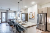 The Everleigh Duluth Type B1 is a thoughtfully designed two-bedroom, two-bathroom residence located in Duluth, GA. The open-concept layout seamlessly connects the kitchen, dining, and living areas, creating a spacious and cohesive flow throughout the home. The kitchen is a standout feature, equipped with stainless steel appliances including a refrigerator, range, microwave, and dishwasher, complemented by sleek granite countertops, a large island with bar seating, warm wood-toned cabinetry, and stylish pendant lighting. Hardwood-style flooring runs throughout the main living areas, adding warmth and continuity. The living room is bright and inviting, with large windows and a glass door that opens to a private balcony, allowing abundant natural light and outdoor views. A ceiling fan adds comfort overhead. Both bedrooms are carpeted and well-proportioned, offering generous natural light through large windows. The bathrooms feature granite vanity tops, wood-toned cabinetry, framed mirrors, and glass-enclosed showers. An in-unit laundry area houses a full-size side-by-side washer and dryer. The overall ambiance is modern and refined, with a neutral color palette and upscale finishes throughout.