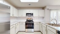This two-story home offers a thoughtfully designed layout spread across two floors, with the majority of the living space on the main level. The open-concept main floor hosts a combined kitchen and living area, two bathrooms, and dedicated closet storage. The kitchen is a standout feature, showcasing white shaker-style cabinetry, marble-look countertops, a classic subway tile backsplash, and a full suite of stainless steel appliances including a gas range, microwave, and refrigerator. A skylight overhead floods the kitchen with natural light, and a peninsula provides additional workspace and seating. The adjacent living room is generously proportioned, featuring plush carpeting, a sleek linear fireplace, a ceiling fan, and multiple windows fitted with blinds that invite abundant natural light. The bathrooms are finished with light tile flooring, white vanity cabinetry, marble-look countertops, and well-lit mirrors. Both bedrooms are carpeted and equipped with ceiling fans; the spacious primary bedroom features vaulted ceilings and a bank of windows. Each bedroom is paired with a dedicated walk-in closet with wire shelving. Carpeted stairs lead to the upper floor, completing this clean, neutral, and move-in-ready home.
