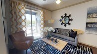 This well-appointed single-floor residence combines contemporary design with functional living across several thoughtfully arranged spaces. The living area serves as the heart of the home, featuring crown molding, wood-style flooring, and a ceiling fan overhead. Bold patterned drapes frame a sliding glass door that opens to a private balcony, filling the space with natural light and outdoor views. A decorative mirror and carefully considered finishes contribute to the room's polished aesthetic.

The kitchen is outfitted with dark, textured cabinetry reaching to the ceiling, complete with a built-in wine rack. Stainless steel appliances—including a French door refrigerator, electric range, and microwave—are paired with a large island featuring a white countertop, undermount sink, and bar seating, all illuminated by pendant lighting.

Both bedrooms offer comfortable proportions, plush carpeting, ceiling fans, and windows with views of the surrounding greenery. The bathroom includes a full soaking tub and shower combination, wood-style flooring, dark upper cabinetry, and clean white fixtures.

A dedicated laundry nook with an in-unit washer adds everyday convenience, completing this cohesive and modern living space.