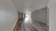 This single-floor residence offers a clean, modern aesthetic throughout, with consistent wood-look flooring and a neutral gray color palette that creates a cohesive and contemporary feel across all rooms. The open living area is a standout feature, showcasing rich dark wood-look flooring, a textured ceiling, and built-in wall shelving ideal for display or storage. A sliding glass door floods the space with natural light and provides direct access to a private outdoor patio area. The kitchen is well-appointed with crisp white cabinetry, marble-look countertops, a subway tile backsplash, stainless steel appliances including a dishwasher and range, and track lighting overhead. A peninsula counter adds additional workspace and a natural division between the kitchen and living areas. The bedrooms are comfortably sized, each featuring wood-look flooring, neutral walls, and windows that bring in natural light. Both bathrooms are finished with marble-style large-format tile surrounds in the tub-shower combinations, white vanities with marble-look countertops, and wood-look flooring, lending a clean and polished look. The space combines practical layout with updated finishes throughout.