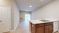 This single-floor residence is designed with a practical, open-concept layout that connects the kitchen and living areas into one cohesive space. The kitchen is equipped with rich medium-toned wood cabinetry, white appliances including a range, dishwasher, and refrigerator, and a double-basin sink set into a light-colored countertop. A peninsula extends into the living area, providing additional workspace and a natural visual divider between the two zones. Light wood-look hard flooring runs throughout the kitchen and living spaces, contributing to a clean, cohesive aesthetic. The living area benefits from a sliding glass door with vertical blinds, allowing natural light to filter in and offering views of the outdoors.

Bedrooms feature neutral-toned carpet, windows with vertical blinds, and closets with built-in shelving and hanging rods. The bathroom includes dark wood cabinetry, a white countertop with an integrated sink, and hard flooring consistent with the rest of the unit. A dedicated laundry area accommodates a full-size washer and dryer. Throughout, neutral gray-beige walls, white trim, and recessed lighting create a bright, move-in ready environment.