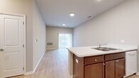 This single-floor residence is designed with a practical, open-concept layout that connects the kitchen and living areas into one cohesive space. The kitchen is equipped with rich medium-toned wood cabinetry, white appliances including a range, dishwasher, and refrigerator, and a double-basin sink set into a light-colored countertop. A peninsula extends into the living area, providing additional workspace and a natural visual divider between the two zones. Light wood-look hard flooring runs throughout the kitchen and living spaces, contributing to a clean, cohesive aesthetic. The living area benefits from a sliding glass door with vertical blinds, allowing natural light to filter in and offering views of the outdoors.

Bedrooms feature neutral-toned carpet, windows with vertical blinds, and closets with built-in shelving and hanging rods. The bathroom includes dark wood cabinetry, a white countertop with an integrated sink, and hard flooring consistent with the rest of the unit. A dedicated laundry area accommodates a full-size washer and dryer. Throughout, neutral gray-beige walls, white trim, and recessed lighting create a bright, move-in ready environment.