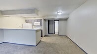 This efficient one-bedroom, one-bathroom unit is thoughtfully laid out across a single floor, making smart use of every square foot. The combined kitchen and living area forms the heart of the space, where soft carpet flows through the living zone while the kitchen transitions to durable hardwood-style flooring. A peninsula counter with a light speckled surface separates the two areas, offering both a prep workspace and a casual dining spot.

The galley-style kitchen is equipped with white appliances including a refrigerator, electric range, and over-the-range microwave, complemented by dark cabinetry above and below. A recessed overhead light keeps the kitchen well-lit. The living area is open and versatile, with neutral walls and a window near the entry that brings in natural light.

The bedroom is a cozy, carpeted retreat featuring a ceiling fan with a light fixture and a window fitted with blinds, allowing for adjustable natural light. The room also includes a secondary door, adding layout flexibility.

The bathroom is clean and functional, with a dark-cabineted vanity topped with a speckled countertop and integrated sink, a large mirror, and a textured accent wall. The entry area features dark interior doors and hardwood-style flooring, creating a defined threshold between the outdoors and the living space.