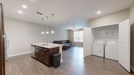 Located at 801 W 4th Ave in Stillwater, Oklahoma, this well-appointed unit offers five bedrooms and three bathrooms across a single thoughtfully designed floor. The open-concept living and kitchen area serves as the heart of the home, featuring durable hardwood-style flooring, recessed lighting, and a ceiling fan that enhances airflow and comfort. The kitchen is outfitted with rich dark cabinetry, granite countertops, stainless steel appliances — including a refrigerator, range, and microwave — and a large island with pendant lighting and bar seating, making it ideal for both cooking and casual dining. The living area benefits from a large window that draws in natural light and offers views of the surrounding neighborhood. Each of the five bedrooms is carpeted for comfort, with neutral wall tones and natural light from individual windows. The primary bedroom provides a generous footprint suitable for a full bedroom suite setup. All three bathrooms are consistently finished with wood-look flooring, dark vanity cabinetry, white countertops, and full tub-shower combinations with chrome fixtures. A dedicated closet adds practical storage. The overall aesthetic is clean, neutral, and functional — well-suited for shared or multi-occupant living.