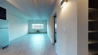 Located at 1525 Yates St in Denver's West Colfax neighborhood, this single-floor unit offers a practical and modern layout across several well-defined spaces. The open-concept living and kitchen area is anchored by light wood-look tile flooring that extends throughout, creating a cohesive and easy-to-maintain surface. Exposed structural beams run across the ceiling, adding an industrial character to the space. The kitchen is well-appointed with dark espresso cabinetry, a classic white subway tile backsplash with decorative accent tiles, stainless steel appliances including a refrigerator and range with overhead ventilation hood, and a stainless steel sink. The living area is generously proportioned, benefiting from natural light through a street-facing window and a wall-mounted lighting fixture. The bedrooms feature plush blue-grey carpeting and dark-trimmed doors, with one bedroom offering access to a dedicated closet. Exposed beam ceilings carry through these rooms as well, maintaining design continuity. The bathroom is finished with floor-to-ceiling grey textured tile surrounding the tub and shower, chrome fixtures, and a sleek ladder-style towel rack, conveying a clean and contemporary aesthetic throughout the unit.