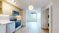 Located in Montréal's Old Port neighbourhood, this 1-bedroom, 1-bathroom unit at 997 De La Commune offers a thoughtfully designed open-concept layout with clean, modern finishes throughout. Light hardwood flooring flows seamlessly across the living, dining, and kitchen areas, creating a bright and cohesive feel.

The kitchen is well-appointed with stainless steel appliances — including a refrigerator, electric range, built-in microwave, and dishwasher — complemented by light wood upper cabinetry, white lower cabinets, a white subway tile backsplash, and ample storage. A globe pendant light and track lighting add functional style to the space.

The living area is bathed in natural light from large windows that frame impressive views of the Montréal skyline and waterfront. The bedroom offers a cozy, private retreat with its own closet and tall windows that continue the expansive city and green space views.

The bathroom features a clean, spa-inspired design with large-format grey floor tiles, a deep soaking tub with shower, a floating wood-tone vanity with an integrated white sink, and a mirrored medicine cabinet. The overall ambiance of the unit is bright, contemporary, and efficiently designed.